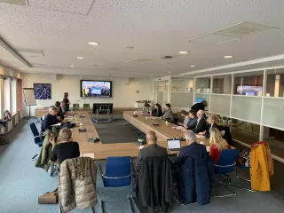 Een zaal met mensen aan tafel, kijken naar een presentatie